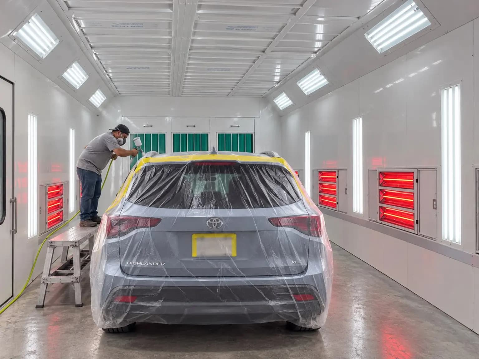 Painter spraying an SUV inside the shop's downdraft paint booth with infrared curing lamps